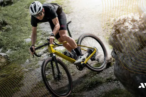 Kolarz na żółtym rowerze gravel pokonuje kamienisty szlak. To właśnie gravel, czyli rower do jazdy po różnym terenie.