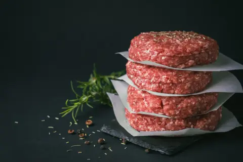 Stos surowych kotletów na burgery, idealne mięso na burgery, z gałązką rozmarynu i pieprzem w tle.