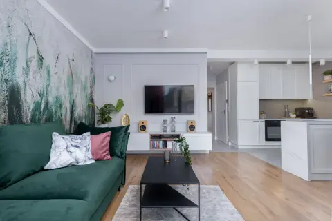 Nowoczesny pokój z telewizorem, zieloną kanapą i designerską tapetą. W tle widać kuchnię.