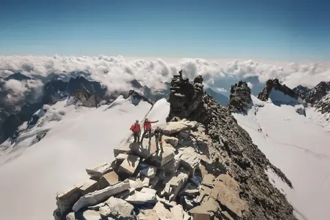 Des alpinistes atteignent le sommet rocheux, dominant un océan de nuages. Un panorama à couper le souffle, un véritable grand paradis.