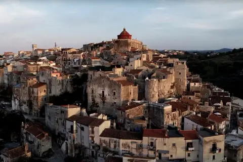 Antico borgo di Vico del Gargano, con case in pietra e tetti rossi che si aggrappano alla collina, dominato da una chiesa con cupola rossa.
