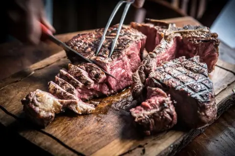 Una succulenta fiorentina steak, tagliata al sangue su un tagliere di legno rustico, con un coltello che affonda nella carne.