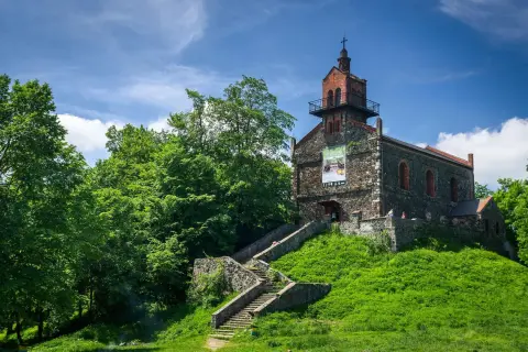 Kamienny kościół na wzgórzu, z kamiennymi schodami prowadzącymi do wejścia. Wokół bujna zieleń, idealne miejsce na odkrywanie dzierżoniów atrakcje.