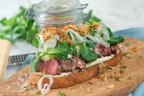 En läcker steak sandwich med mört kött, krispig sallad, lök och parmesan på rostat bröd.