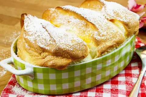 Ein goldbrauner, luftiger Salzburger Nockerl-Auflauf, bestäubt mit Puderzucker, in einer grünen Karamikform.