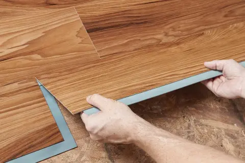 Hands installing wood-look vinyl plank flooring. Once installed, you can walk on vinyl plank flooring immediately.