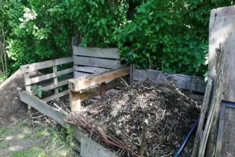 Drewniany kompostownik z pryzmą materiału organicznego w ogrodzie.