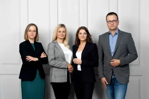 Cztery osoby w strojach biznesowych stoją obok siebie na jasnym tle.