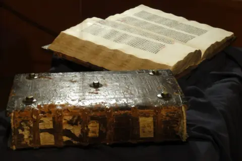 Stary, zniszczony księgozbiór w stylu biblijnym, z metalowymi okuciami i otwartą księgą pełną tekstu.