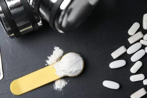 Bilancia, pillole e polvere bianca su un cucchiaio: cosa è meglio, proteine o aminoacidi per aumentare massa?