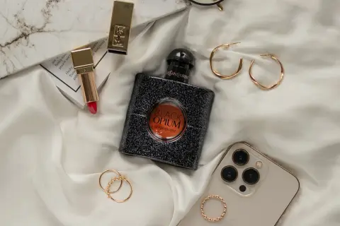 Elegancka kompozycja z flakonem perfum **black opium**, złotą szminką, pierścionkami i telefonem.