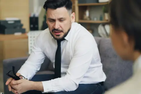 Mężczyzna w białej koszuli i krawacie, trzymający okulary, zastanawia się, jak inteligentnie zakończyć rozmowę.