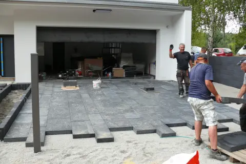 Budowa podjazdu z ciemnych płyt betonowych przed nowoczesnym budynkiem.