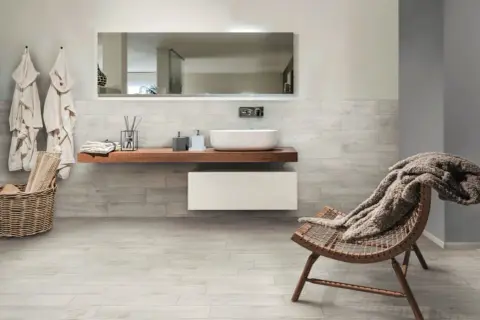 Salle de bain moderne avec murs et sol en grès cérame émaillé effet bois, lavabo suspendu, fauteuil confortable.