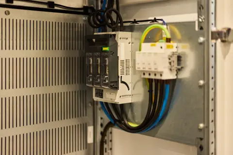 Wnętrze szafy elektrycznej z bezpiecznikami i przewodami. Sprawdź, jak sprawdzić czy falownik działa, analizując połączenia i wskaźniki.