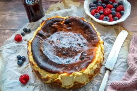 Ein perfekt gebackener San Sebastian Cheesecake mit karamellisierter Kruste, garniert mit frischen Beeren und einem Glas Marmelade.