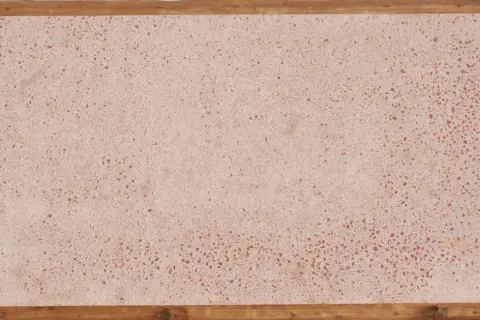Superficie in coccio pesto con venature rosse, incorniciata da listelli di legno grezzo.