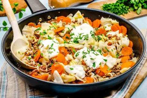 Herzhaftes spitzkohl mit hackfleisch in der Pfanne, garniert mit Klecksen saurer Sahne und Petersilie. Ein deftiges Gericht!
