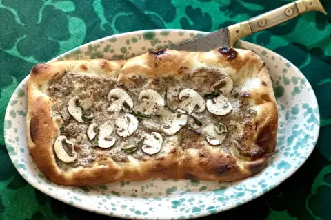 En gyllene pinsa med svamp och örter, redo att skäras med en kniv. Ett perfekt pinsa recept för en mysig kväll.