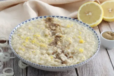 Un cremoso risotto alla liquirizia, guarnito con scorza di limone e una spolverata di polvere scura, pronto per essere gustato.