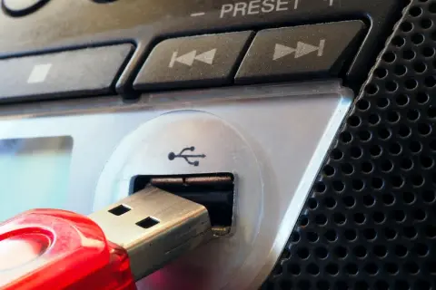 Czerwony pendrive podłączony do portu USB urządzenia. Widoczne przyciski sterowania i głośnik. Parowanie danych z pamięci przenośnej.