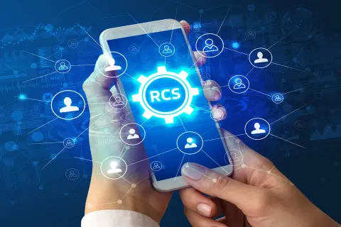 Dłonie trzymają smartfon z ikoną RCS w centrum, otoczoną siecią połączeń i symboli użytkowników na tle danych.