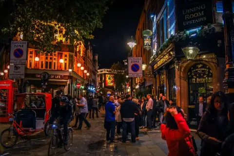 En livlig gata i London på kvällen, med folk som minglar utanför pubar och restauranger, som påminner om stadens nattklubbar.