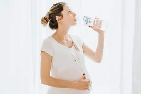 Une femme enceinte boit de l'eau d'une bouteille, prenant soin de son hydratation.