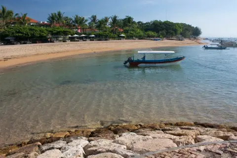 Spokojna plaża w Sanur z łodzią "Water Walk" kołyszącą się na turkusowej wodzie.