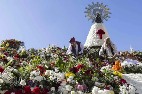 Ofrenda de flores a la Virgen del Pilar. Hombres colocan flores en una estructura adornada con la imagen de la Virgen.