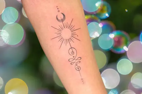 Brazo con tatuaje de sol, luna y símbolo unamalo, representando protección y tatuajes espirituales.