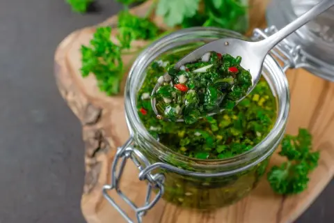 Łyżka z aromatycznym chimichurri, pełnym ziół i chili, nad słoikiem pełnym tej zielonej, pysznej pasty.