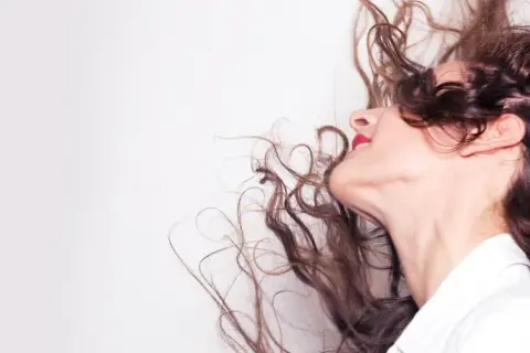Frauenkopf mit wallenden, braunen Locken, die sich im Wind bewegen. Tipps, wie man locken richtig pflegt, um diesen Schwung zu erhalten.