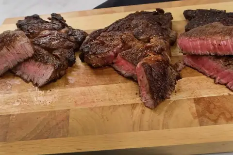 Tre saftiga steak minute-biffar, perfekt stekta med rosa kärna, ligger på en träskärbräda.