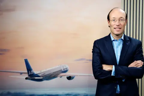 SAS VD, en man i kostym, står framför en bild av ett flygplan i solnedgången.