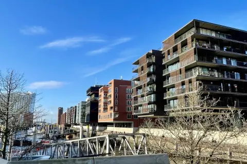 Moderne Gebäude mit Balkonen säumen das Wasser, wo Boote liegen. Die Magellan Terrassen bieten einen Blick auf die Hafencity.
