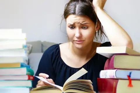 Joven con libros apilados, pensativa, buscando qué hacer cuando te aburres.
