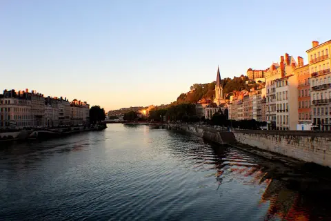 Vue de Lyon au coucher du soleil, avec le Rhône et ses quais bordés d'immeubles. La descente du Rhône offre un spectacle paisible.