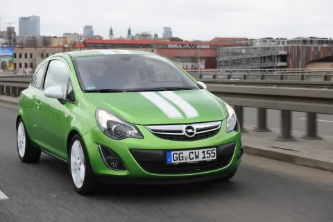 Zielony Opel Corsa D z białymi pasami na masce, z nowymi żarówkami w reflektorach, jedzie po moście.