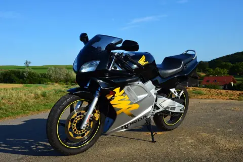 Czarny motocykl Honda NSR z żółtymi akcentami na tle zielonych pól i błękitnego nieba.