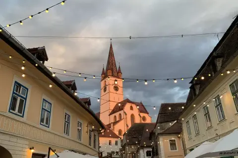 En charmig europeisk stad med en kyrktorn i bakgrunden, kantad av hus och ljusslingor. Perfekt för en resa till billigaste landet i Europa.