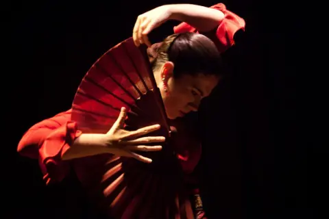 Bailarina de flamenco con un abanico rojo, evocando la pasión de la guajira.