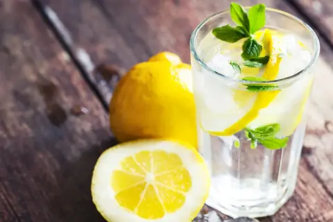 Erfrischendes zitronen wasser mit Eis und Minze, daneben ganze und halbierte Zitronen auf rustikalem Holz.