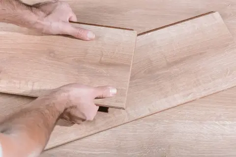Man's hands fitting a new laminate plank to replace damaged parquet.