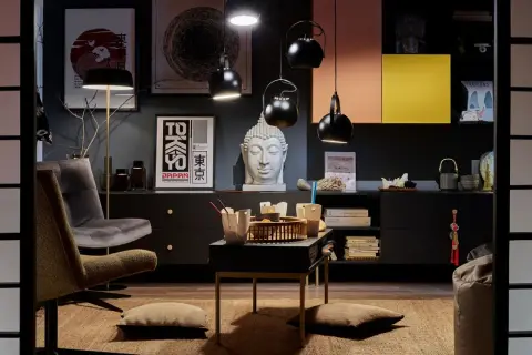 Salon w stylu eklektycznym: szara sofa, fotel, stolik z bambusową tacą, głowa Buddy, plakaty z Japonii i Azji.