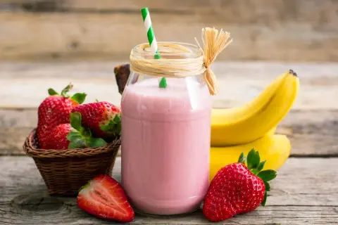 Pyszny koktajl truskawkowo bananowy w słoiku, obok świeże owoce i słomka. Idealny na orzeźwienie!