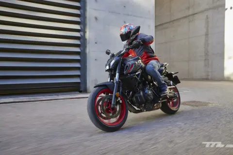 Motociclista con casco y chaqueta roja y gris conduce una Yamaha MT-07 negra con detalles rojos por una calle urbana.