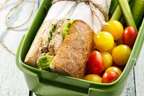 Pyszna kanapka z kurczakiem, świeże pomidorki i ogórek w zielonym pudełku na lunch.