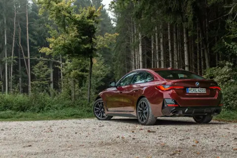 Ciemnoczerwone BMW Gran Coupé na szutrowej drodze w lesie.