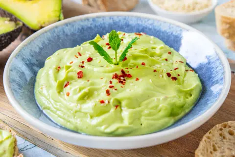 Cremige Avocado-Creme, garniert mit Minze, Sesam und Chiliflocken, serviert in einer blauen Schüssel.